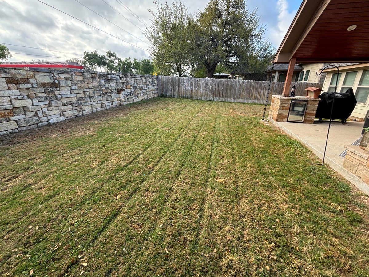 Spacious backyard with newly seeded lawn, brick wall, wooden fence, patio, and brick house with covered area